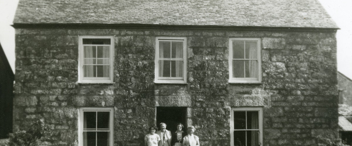 An old photograph of a family standing in front of their big stone wall house